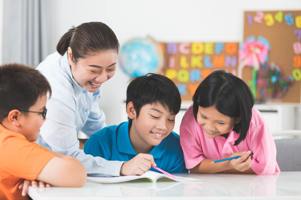 young asian teacher helps young school kids in class.